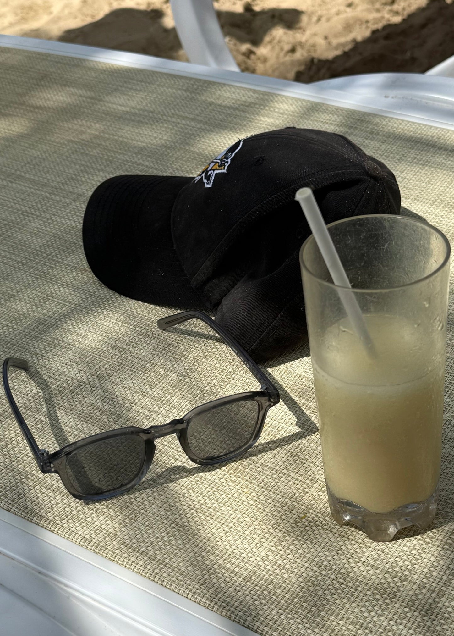 Black sunglasses and cap on a textured surface with a glass of lemonade.